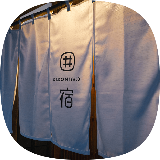 夕暮れ時に灯りに照らされた、KAKOMIYADOの白い暖簾